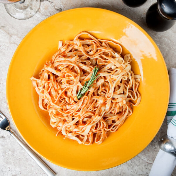 A plate of pasta with sauce and a fork in a Libbey saffron porcelain pasta bowl.