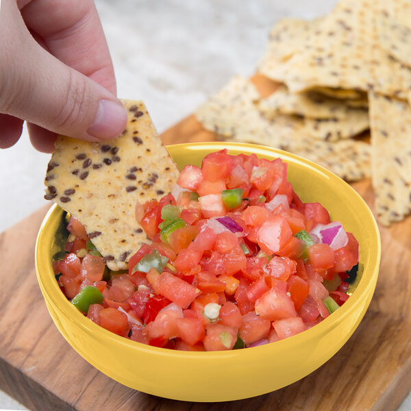A hand holding a chip and dipping it into a bowl of salsa.