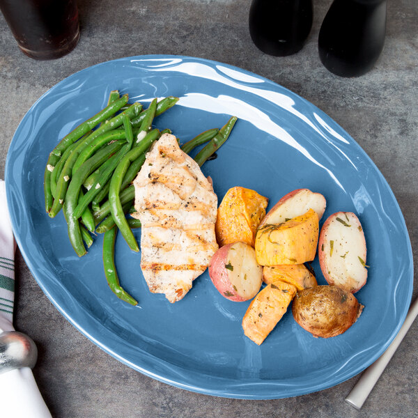 A Libbey blueberry carved porcelain platter with chicken, potatoes, and green beans on a table.