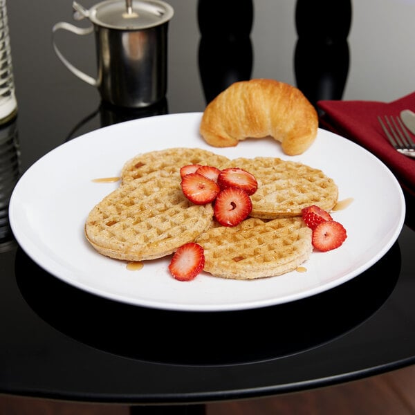 A Carlisle white melamine plate with waffles and strawberries on it on a table.