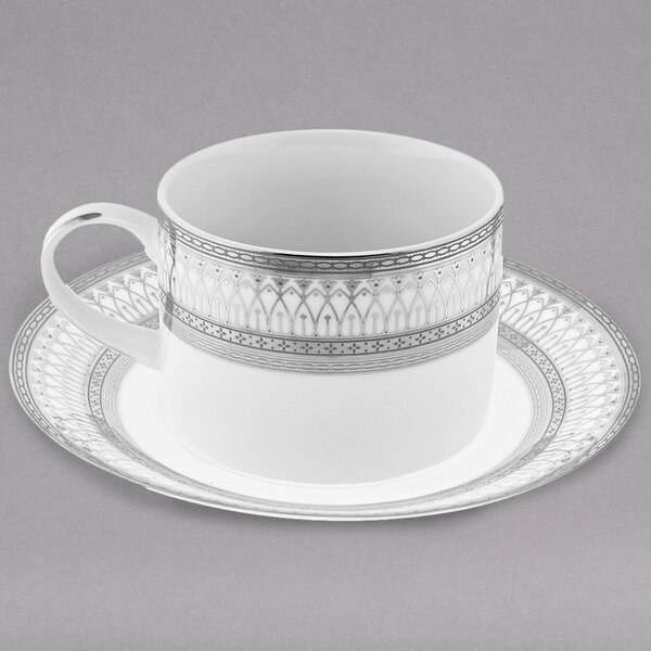 A white porcelain cup and saucer with silver accents and a pattern.