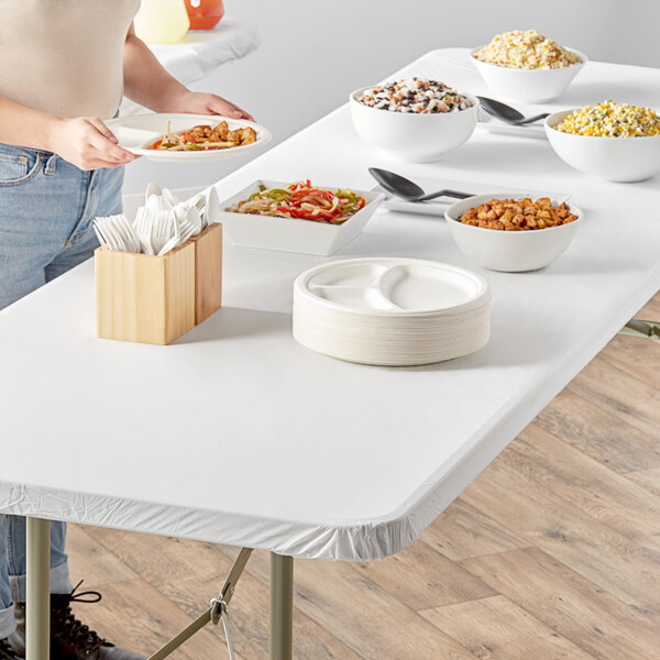 A person standing at a white table with food on plates covered by a white Stay Put tablecloth.