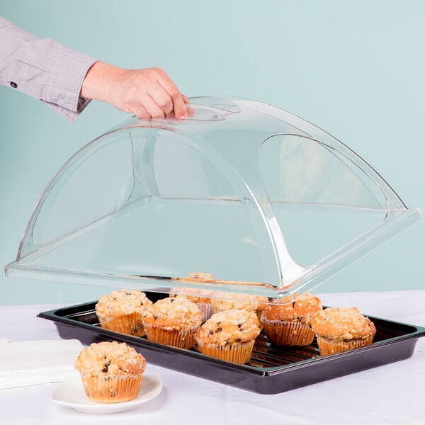 A hand holding a clear container with a tray of muffins on it.