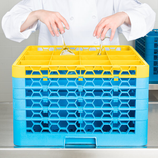 A woman in a white chef's coat using a yellow Carlisle glass rack with blue extenders.