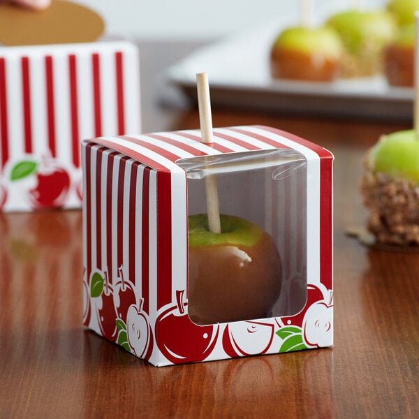 A red and white striped Baker's Mark candy apple box with a window containing a candy apple.