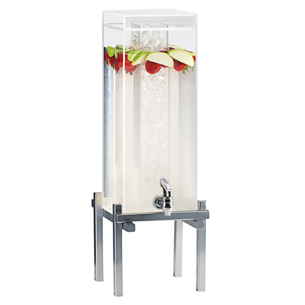 A silver Cal-Mil beverage dispenser with ice chamber and a faucet on a metal stand filled with water and fruit.