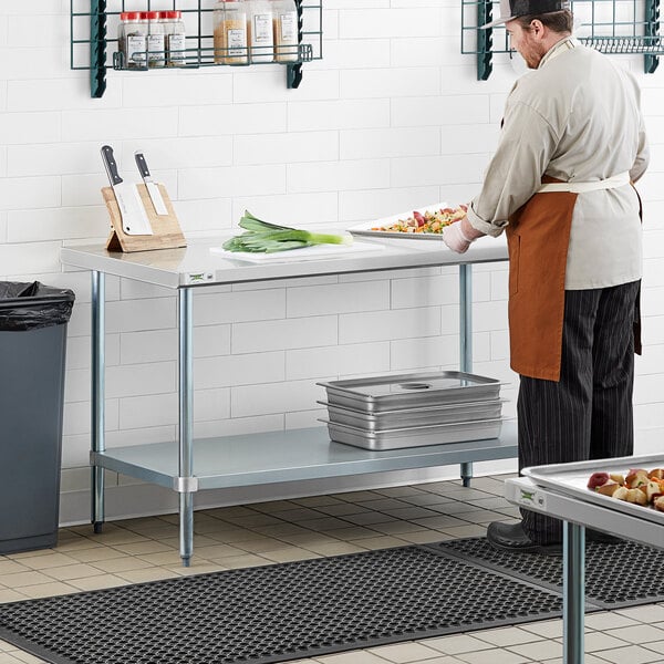 A man in an apron using a Regency stainless steel work table with an undershelf in a kitchen.