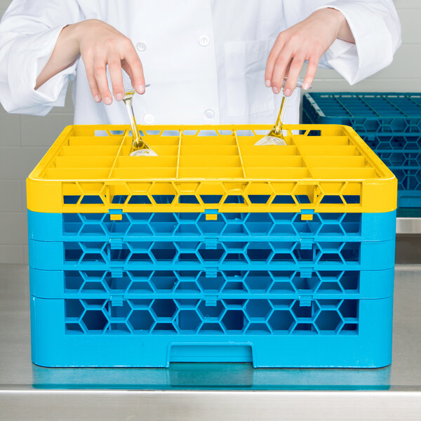 A person holding spoons in a yellow Carlisle glass rack with blue extenders.