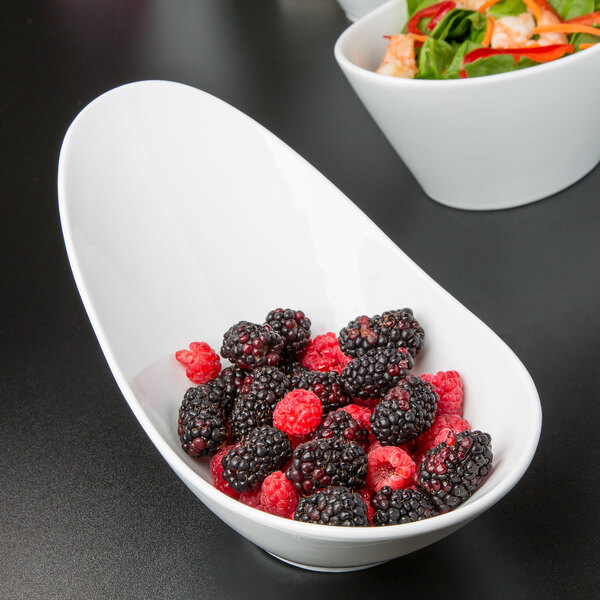 A Libbey ultra bright white porcelain bowl filled with blackberries and raspberries next to a bowl of salad with shrimp and vegetables.