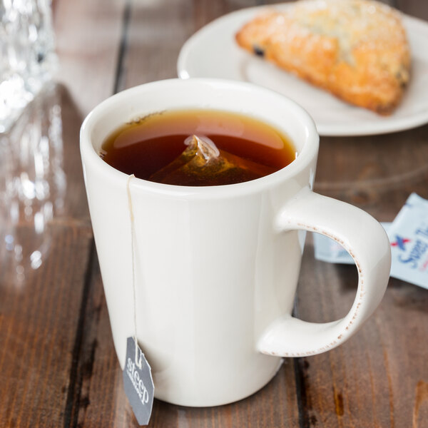 A Libbey ivory porcelain mug filled with tea with a teabag in it on a table.