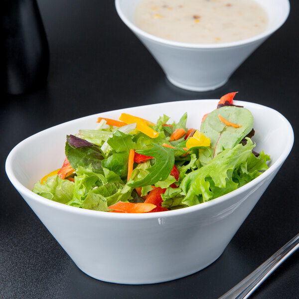 A Libbey white porcelain bowl of salad with a spoon and a bowl of soup.