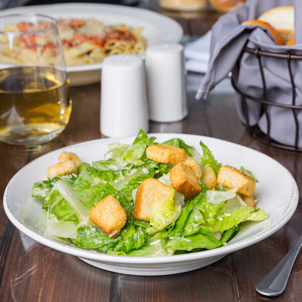 A bowl of salad with croutons on a table.
