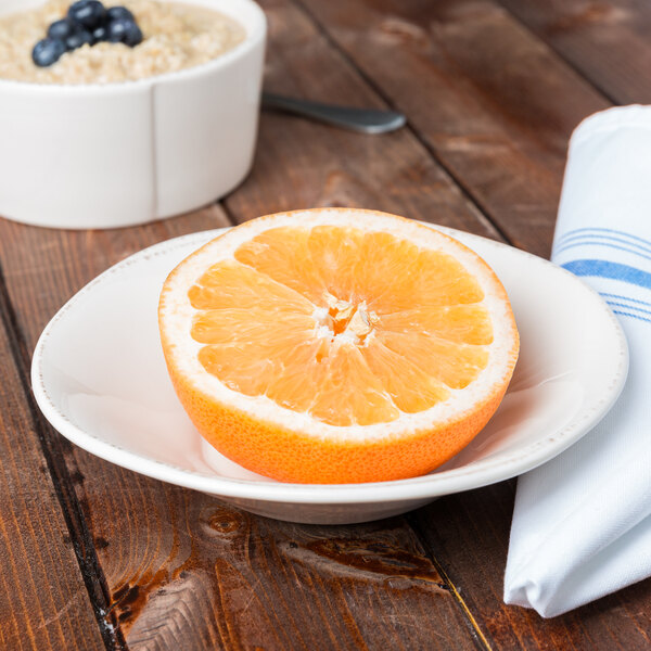 A Libbey Farmhouse ivory porcelain grapefruit bowl filled with oatmeal with a half of an orange on a plate.