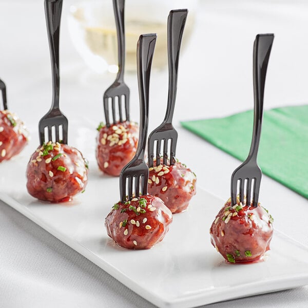 A plate of meatballs with Visions black plastic tasting forks on a table.