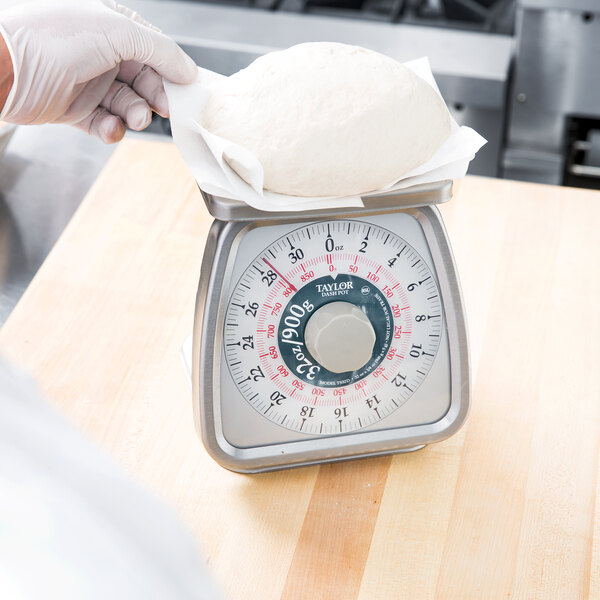 A person using a Taylor mechanical portion scale to weigh dough.