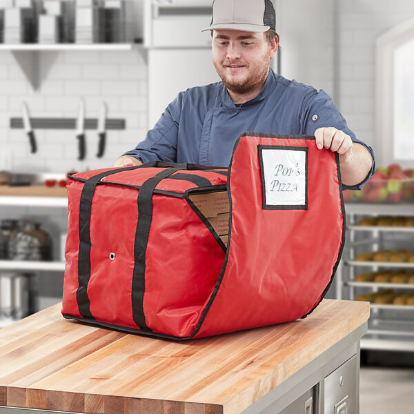 A man in a chef hat opening a red ServIt insulated pizza delivery bag.