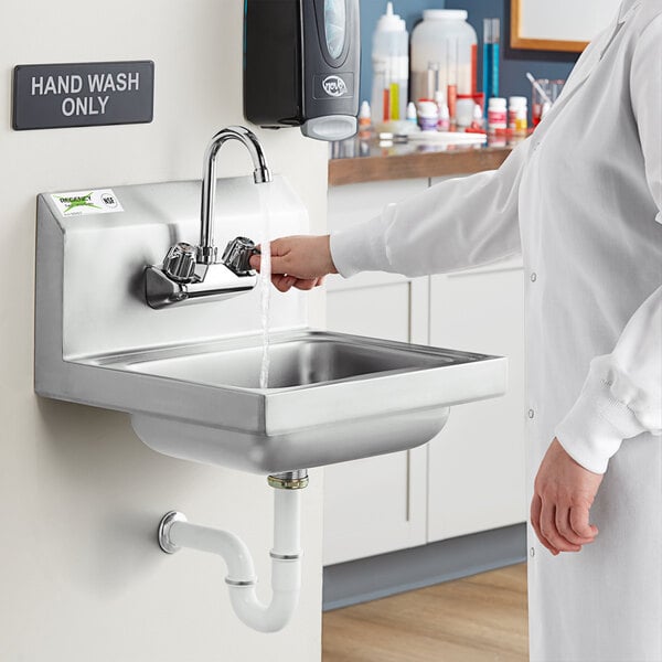 A woman in a lab coat washing her hands in a wall mounted hand sink with a gooseneck faucet.