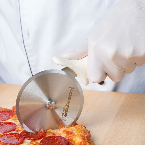 A person using a Dexter-Russell pizza cutter to cut a pizza.