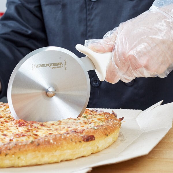 A person uses a Dexter Russell Sani-Safe Pizza Cutter to cut a pizza.