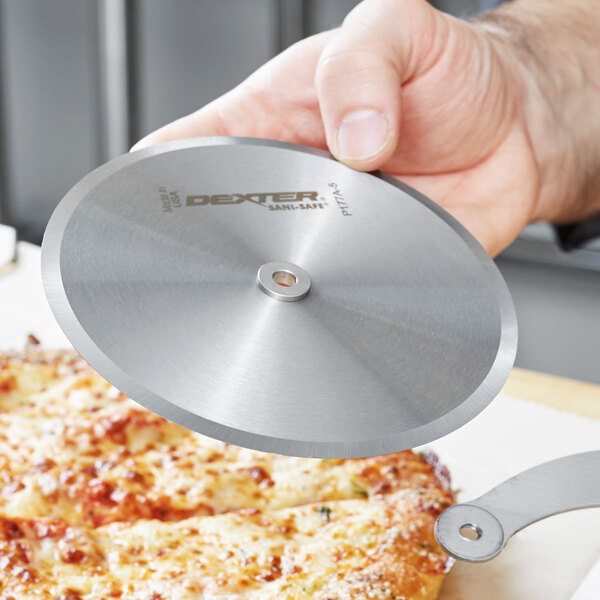 A hand holding a Dexter-Russell circular pizza cutter blade over a pizza.