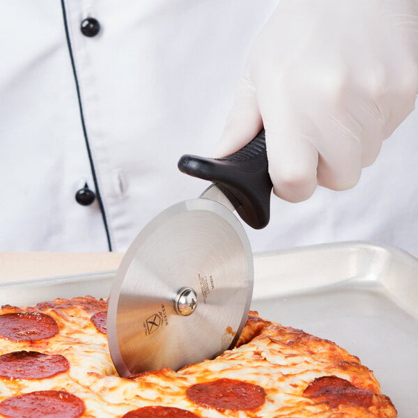 A hand in a white glove uses a Mercer Culinary Millennia pizza cutter with a black handle to cut a pizza.