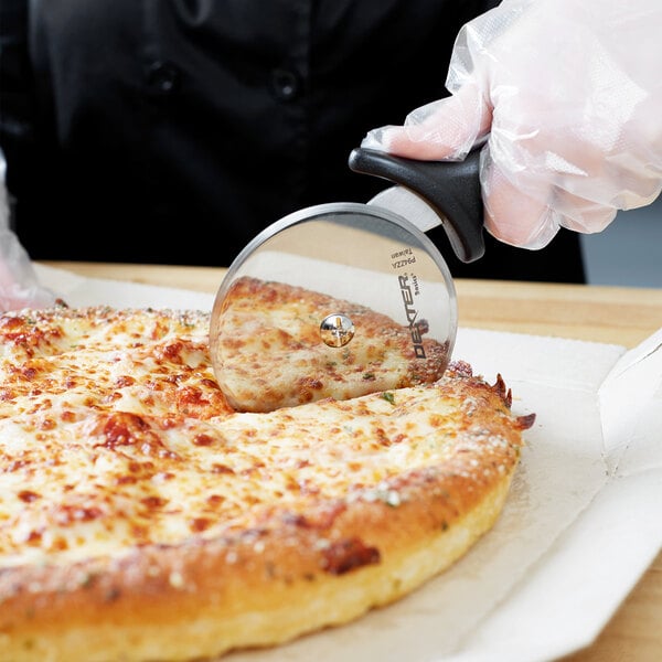 A person using a Dexter-Russell pizza cutter to cut a slice of cheese pizza.