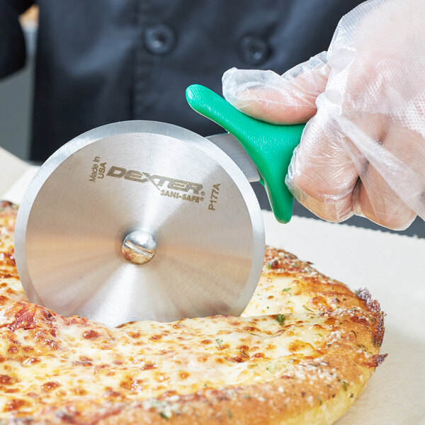 A person in a plastic glove cutting a pizza with a Dexter-Russell green handled pizza cutter.