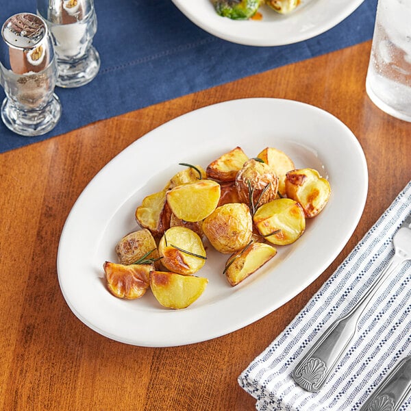 A plate of potatoes on an Acopa Bright White oval platter with a fork and knife.