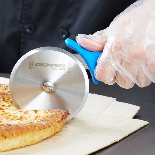 A person using a Dexter-Russell blue handled pizza cutter to cut a pizza.