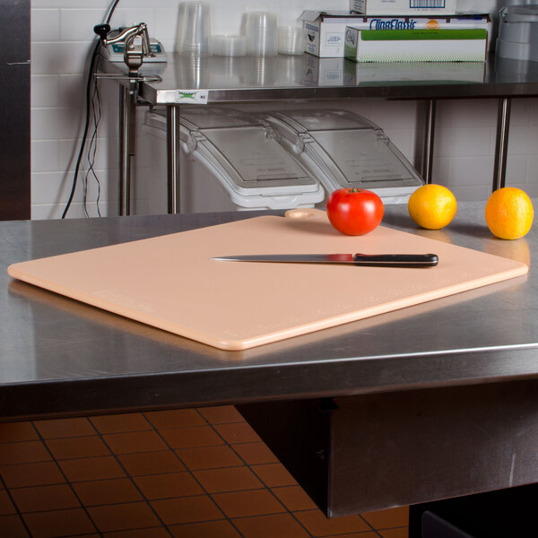 A San Jamar brown cutting board with a knife on a table with tomatoes and oranges.