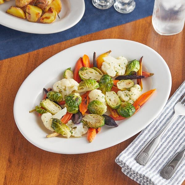 An Acopa Bright White wide rim stoneware platter with vegetables on a table.