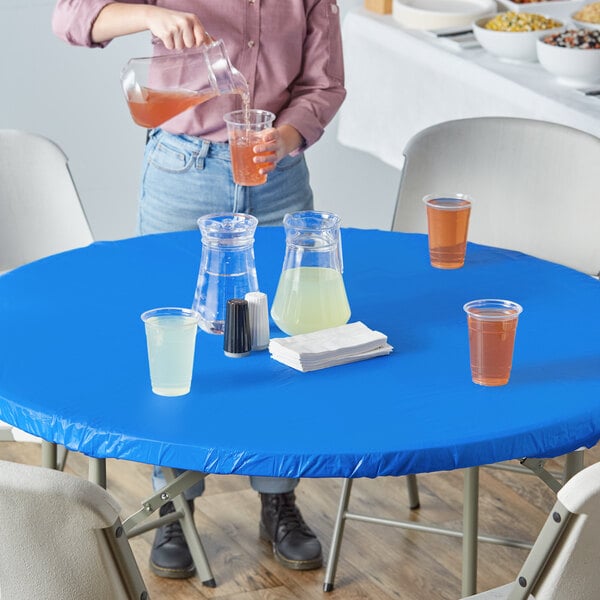 A woman pouring a brown drink into a plastic cup on a blue table with a Royal Blue Stay Put plastic tablecloth.