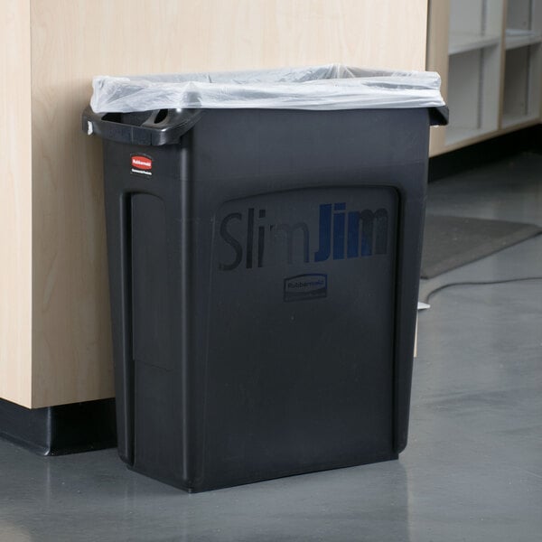 A black Rubbermaid Slim Jim trash can with a plastic bag over it.