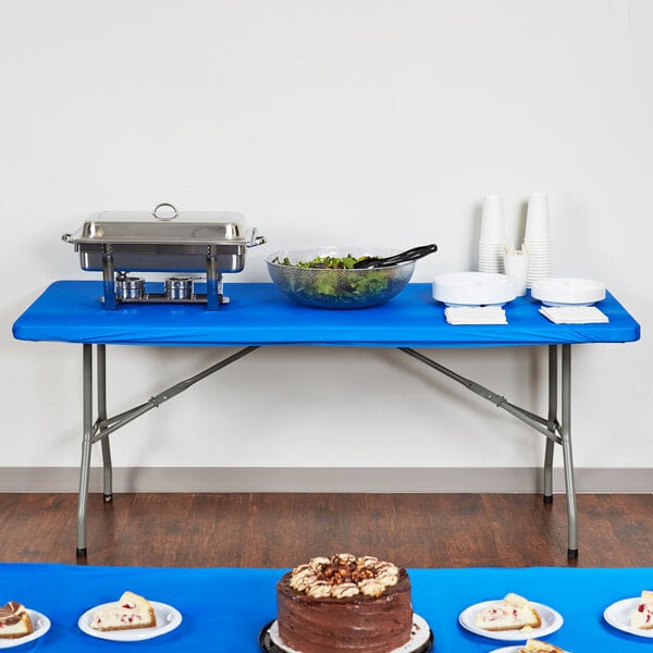 A table covered with a Creative Converting royal blue plastic tablecloth with food on it.
