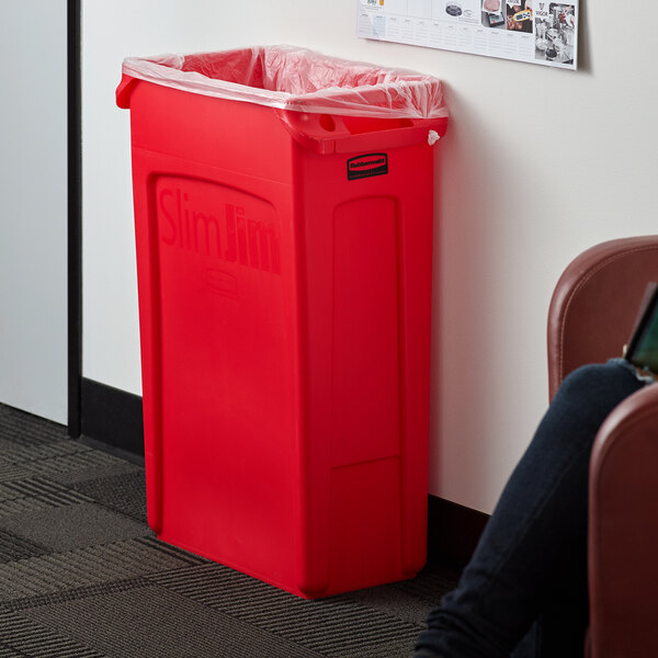 A woman sitting in a corporate office cafeteria next to a red Rubbermaid Slim Jim trash can.
