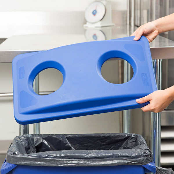 A person holding a blue Rubbermaid Slim Jim recycling bin lid with holes.