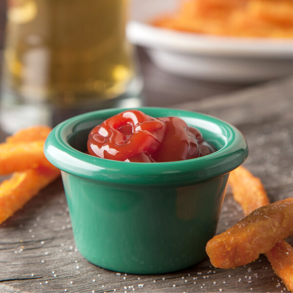 A Carlisle green smooth melamine ramekin filled with ketchup next to a bowl of french fries.