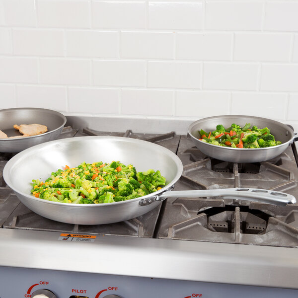 A Vollrath Wear-Ever aluminum fry pan with vegetables cooking on a stove.