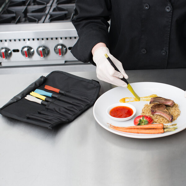 A hand in gloves using a yellow silicone brush to plate food.