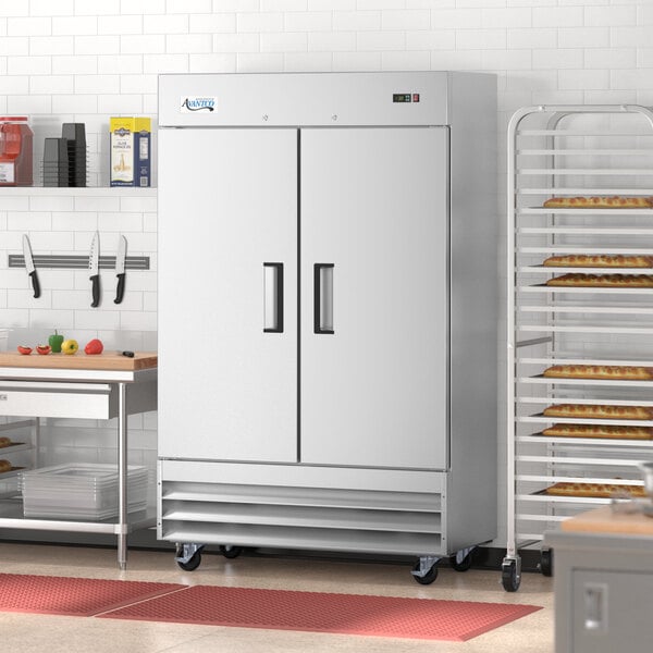A white Avantco reach-in freezer with black handles in a large school kitchen.