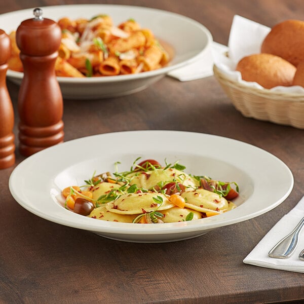 An Acopa ivory pasta bowl filled with pasta on a table with bread and wine.