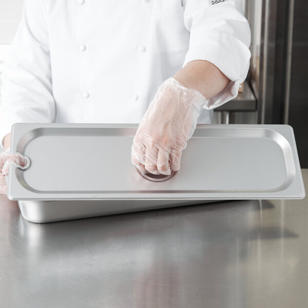 A person wearing gloves holding a Choice stainless steel steam table pan cover over a tray.