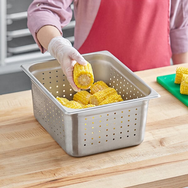 A person putting corn on the cob in a Choice 1/2 Size stainless steel perforated hotel pan.
