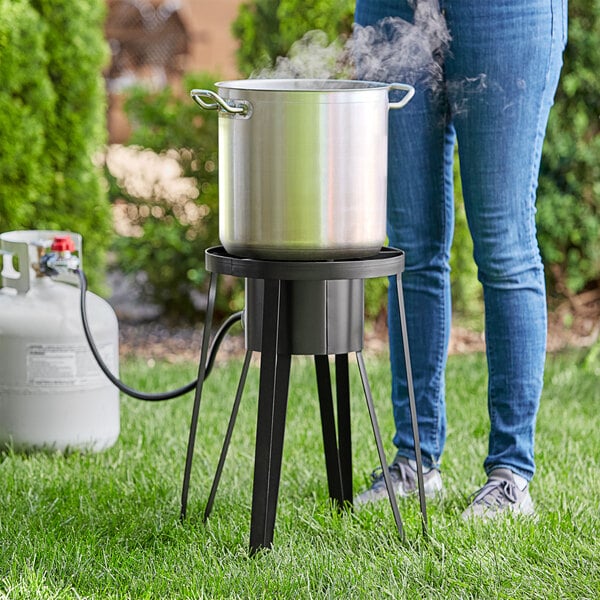 A woman standing next to a large metal pot on a Backyard Pro outdoor gas stove.