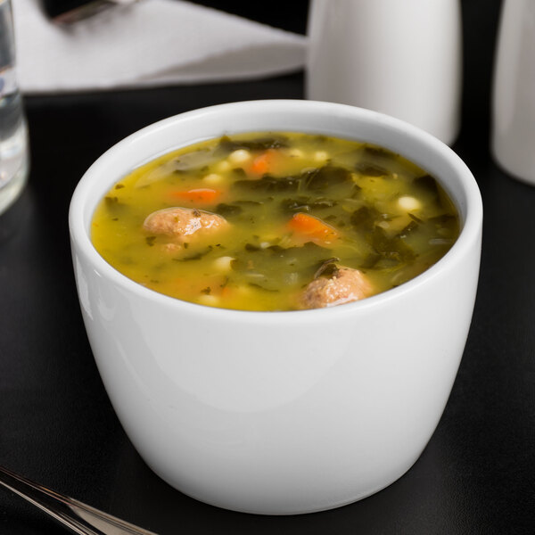 A Libbey Royal Rideau white porcelain bouillon bowl filled with soup with vegetables and meatballs.