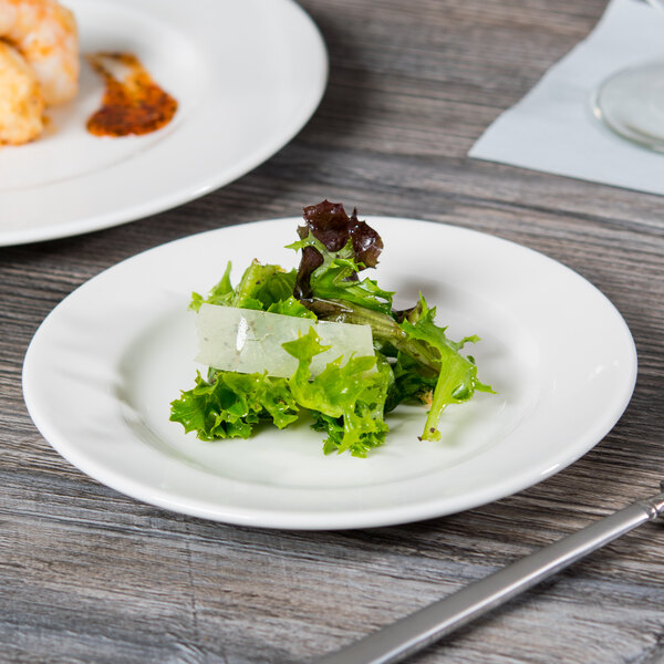 A Libbey white wide rim porcelain plate with a green salad on it on a table.