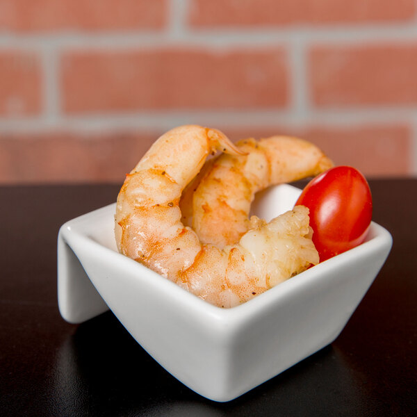 A shrimp and cherry tomato in a square white bowl.