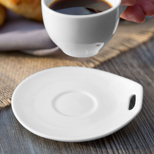 A hand pouring coffee into a Libbey Royal Rideau white porcelain saucer.