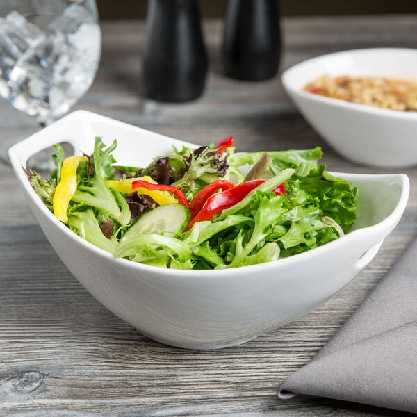 A bowl of salad in a white Libbey porcelain bowl with handles on a table.