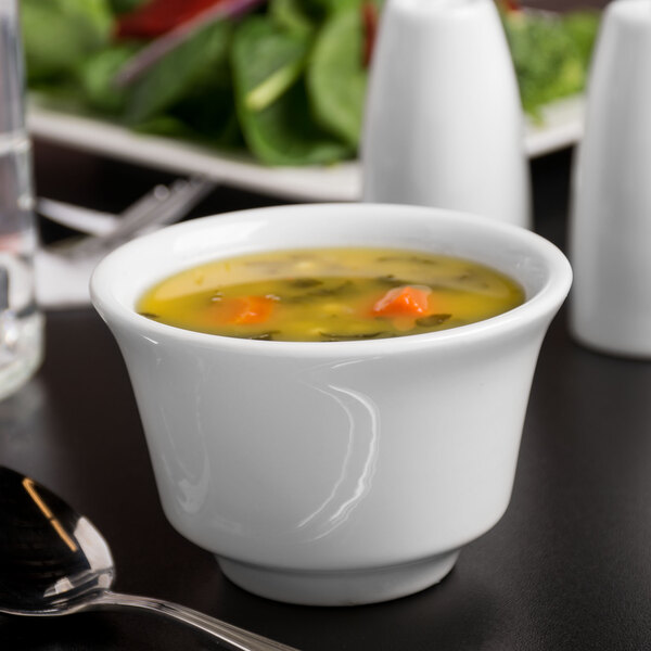 A Libbey white porcelain bouillon bowl filled with soup with a spoon next to it.